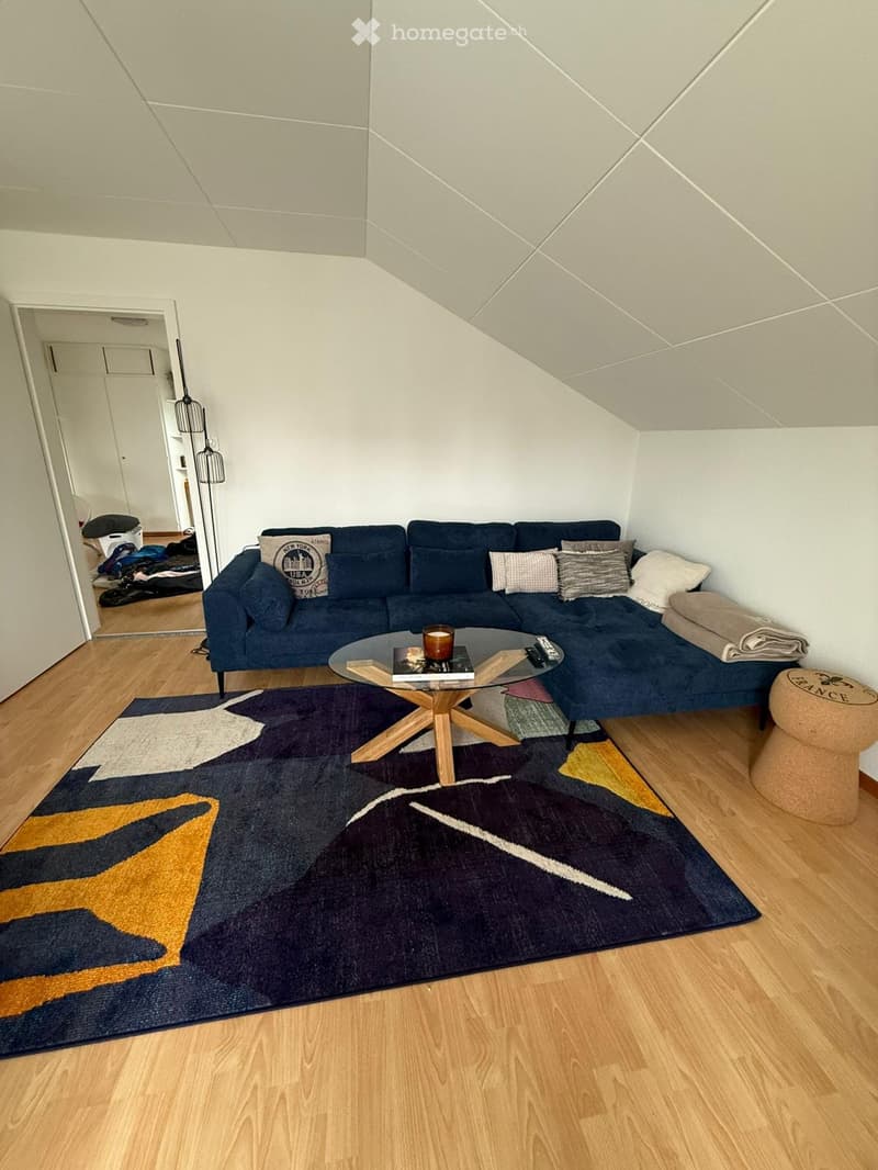 Living room with a blue sectional sofa, glass coffee table, wooden floor, and colorful rug.