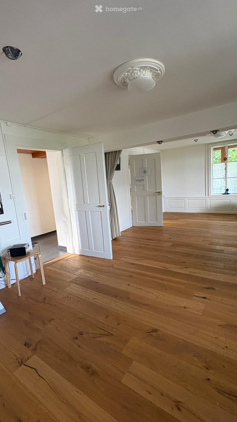 Empty room with wooden flooring, white walls, and several doors leading to other spaces. A small table with a black box is visible near the left wall.