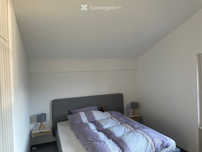 Bedroom with a grey headboard, white bed frame, purple bedding, two nightstands with lamps, and a small bottle on one nightstand.