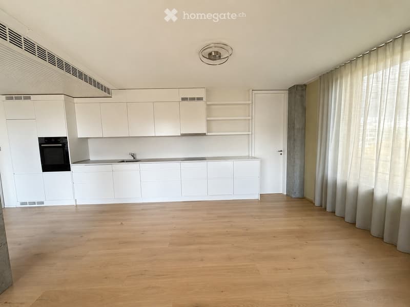 Empty kitchen with white cabinets, wooden floor, and large windows with curtains. No furniture or appliances visible.