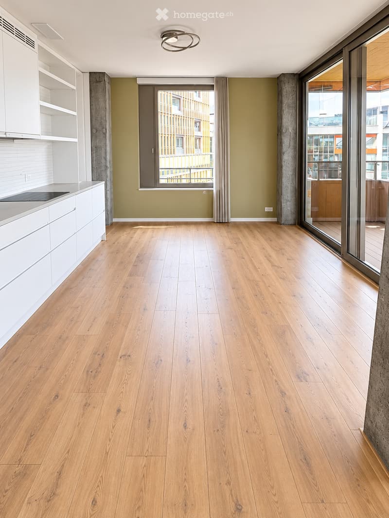 Empty room with light wooden flooring, white cabinetry, and large windows with views of the city.