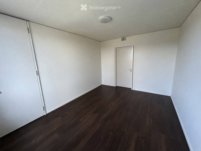 Empty room with white walls, dark wooden flooring, and a single white door.