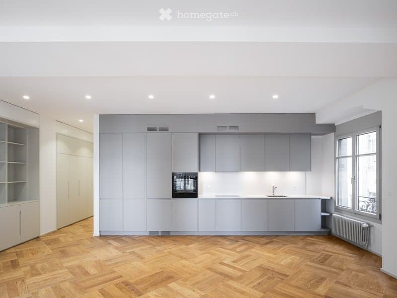 Modern kitchen with grey cabinets, wooden herringbone floor, built-in oven, and sink.
