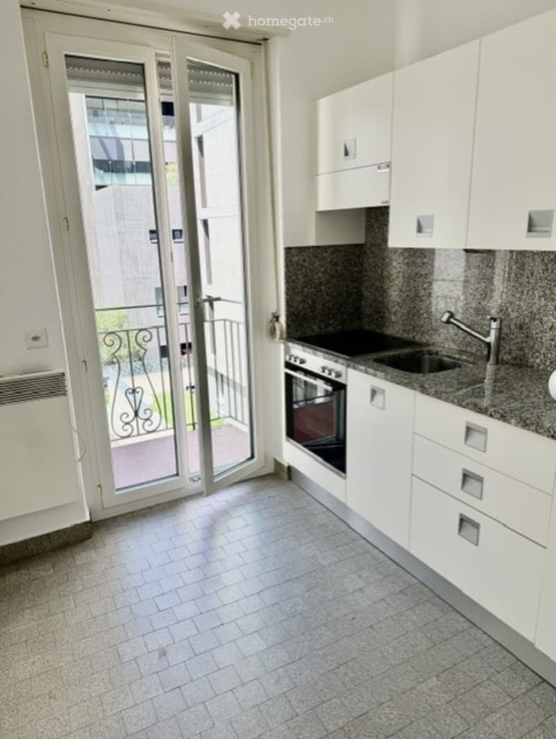 Modern kitchen with white cabinets, granite countertops, built-in oven, and a large sliding glass door leading to a balcony.