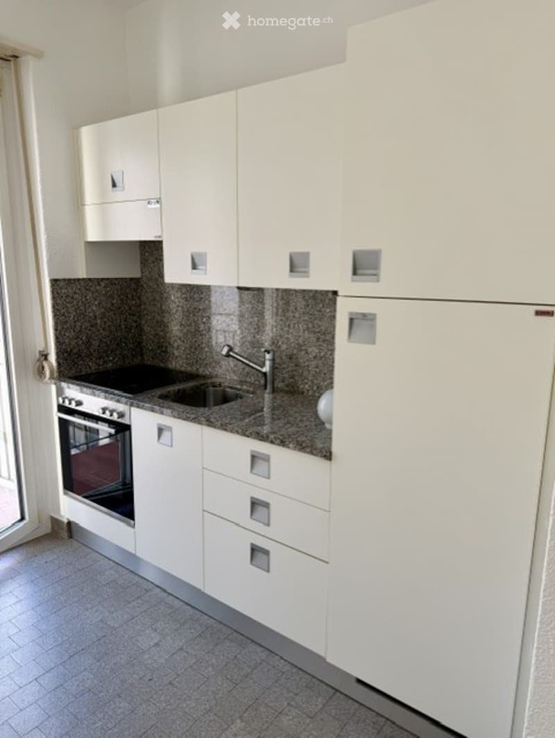 Modern kitchen with white cabinets, granite countertop, stainless steel sink and faucet, built-in oven, and refrigerator.