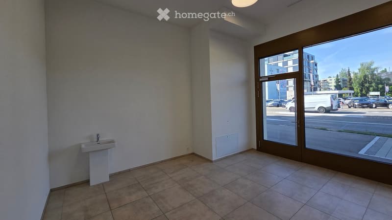 Empty room with tiled floor, white walls, a small sink, and large glass doors leading to a parking area.