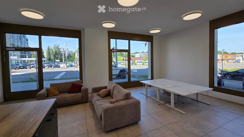 Modern, well-lit room with large windows, two sofas, a table, and chairs. The space is clean and organized, with a view of the street outside.