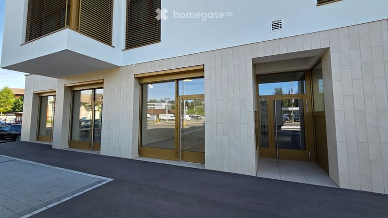 Modern building entrance with glass and wood doors, light-colored tiled facade, and a raised ground floor area.