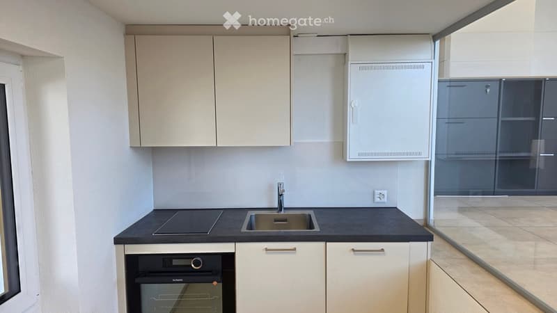Modern kitchen with white cabinets, black countertop, sink, faucet, and built-in oven.