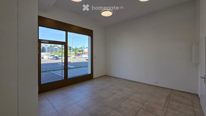 Empty room with tiled floor, white walls, and a large glass door leading to a parking area.