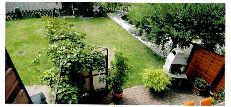 Well-maintained garden with a lawn, a brick pathway, a barbecue, and various plants and shrubs.