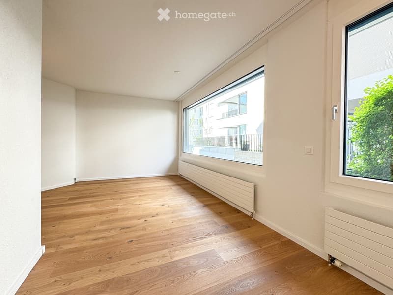 Empty room with light wooden flooring, white walls, large windows, and radiators along the walls.