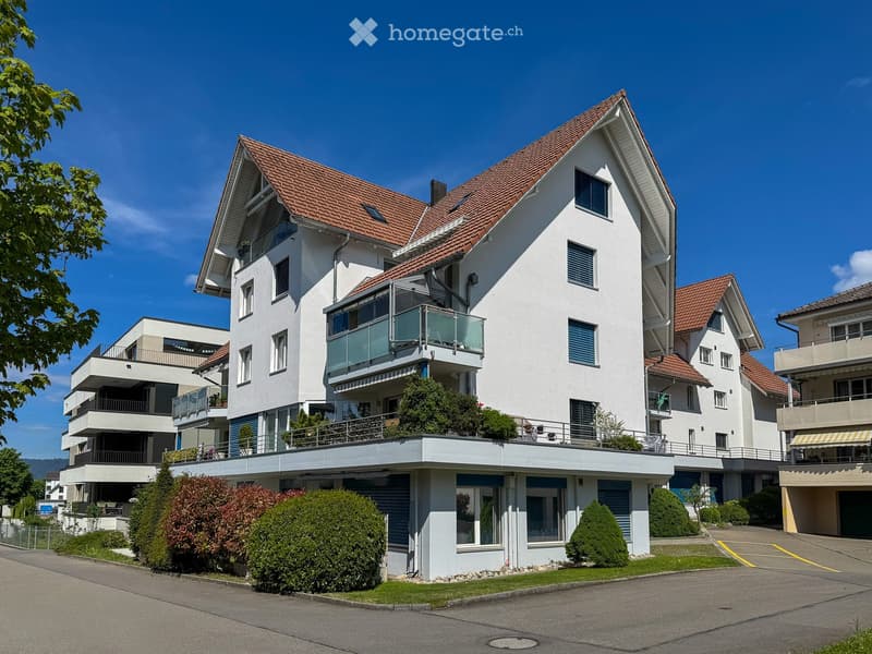 Modern multi-story house with white exterior, red-tiled roof, multiple balconies, and surrounding greenery.