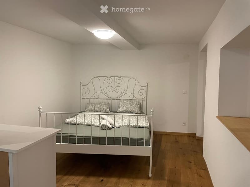 Cozy bedroom with a white metal bed, patterned bedding, and a wooden nightstand.