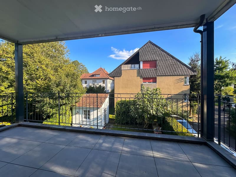 Balcony with tiled floor, metal railing, and view of neighboring houses and greenery.