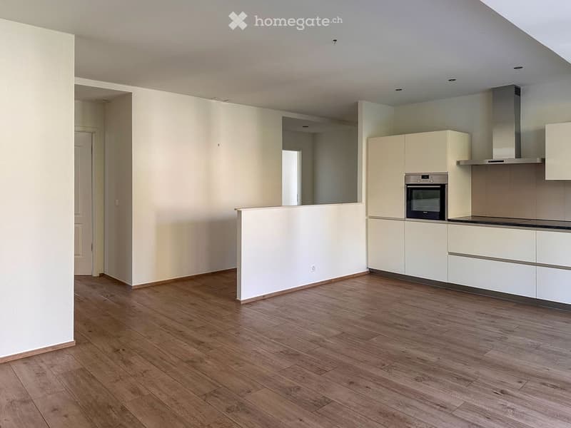 Empty kitchen with white cabinets, wooden flooring, and a built-in oven. No furniture or appliances are present.