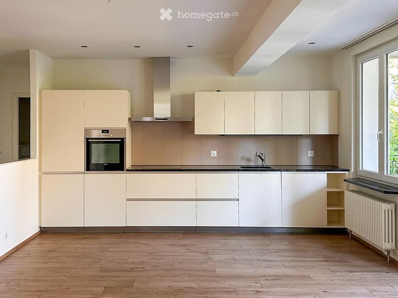 Modern kitchen with light-colored cabinets, wooden flooring, and built-in appliances including an oven and sink.