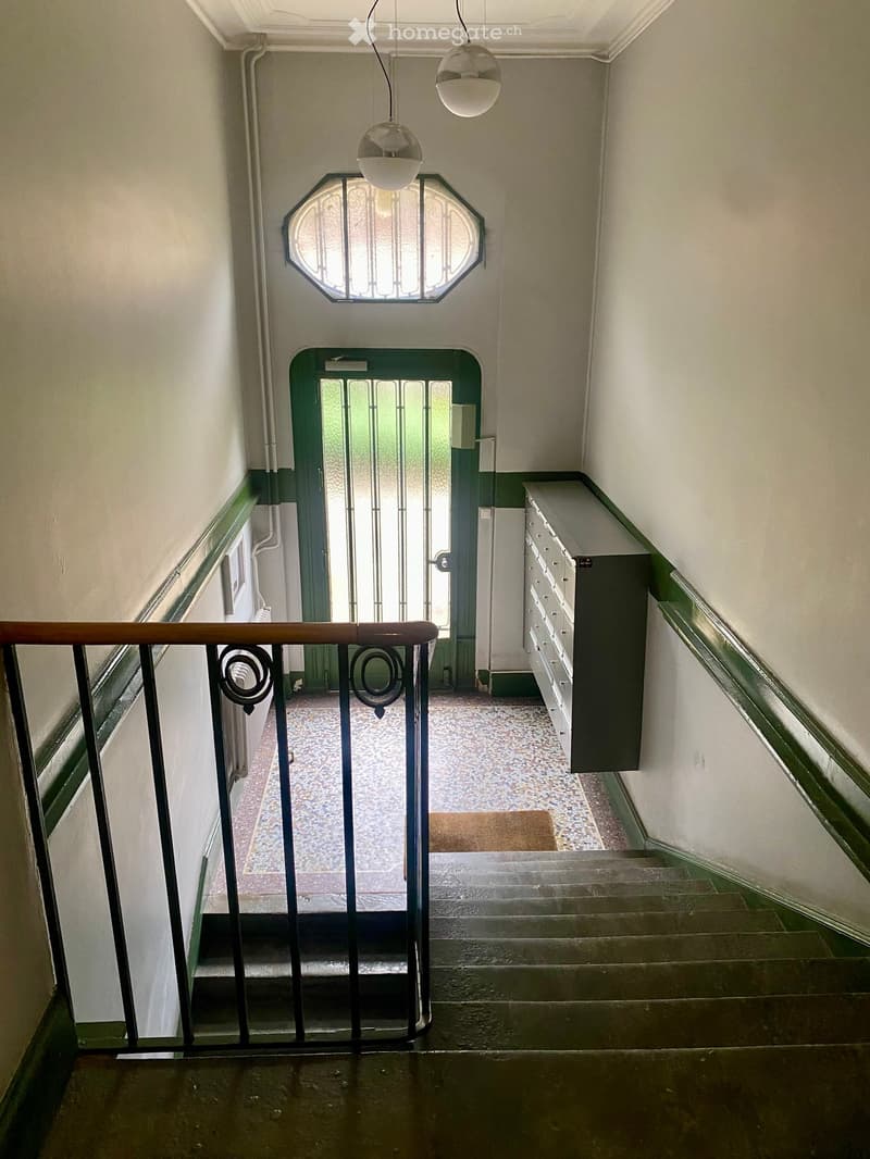 Staircase with wooden handrail, metal balustrade, and decorative octagonal window above. Green door at the end of the hallway with a small rug in front.