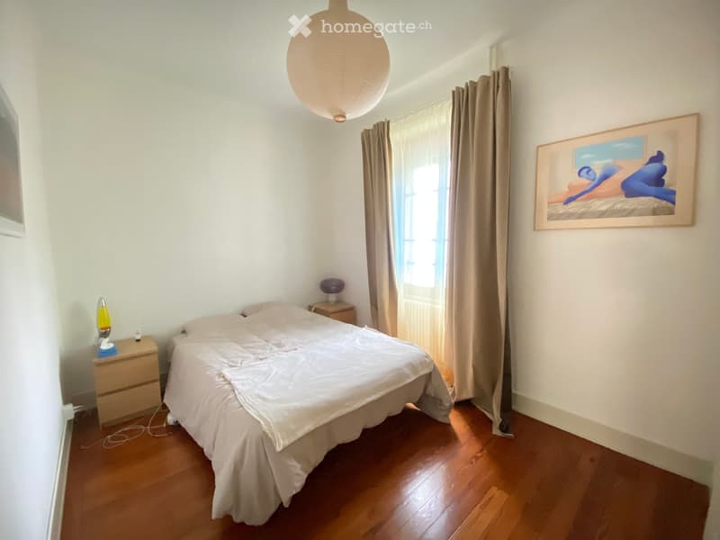 Cozy bedroom with wooden flooring, a neatly made bed, nightstands with lamps, and a large abstract painting on the wall.