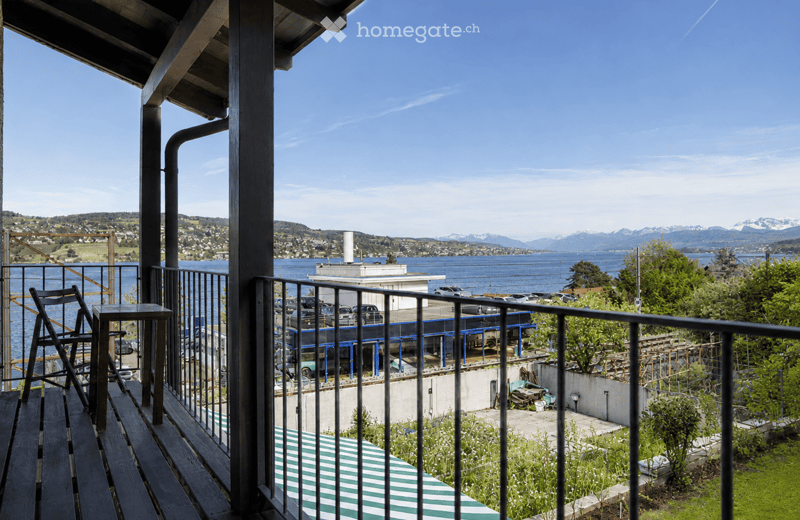 Balcony with wooden decking, metal railing, and scenic view of water and distant mountains.