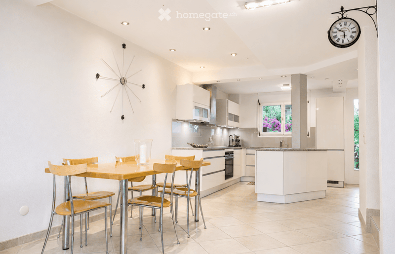 Modern kitchen with white cabinets, a dining area, and a coffee machine on the counter.