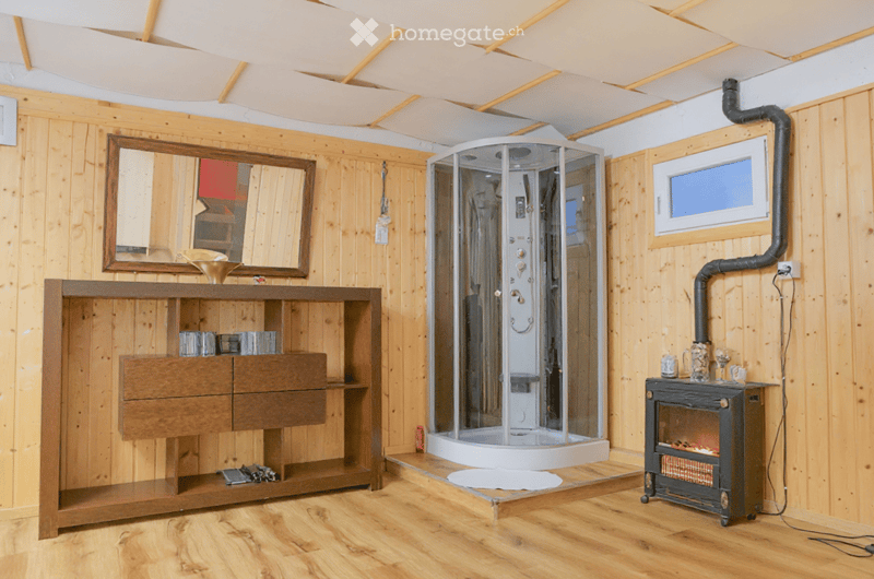 Bathroom with wooden walls and floor, featuring a large mirror, wooden vanity with drawers, a modern glass-enclosed shower stall, and a small wood-burning fireplace.