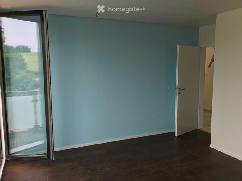 Empty room with light blue walls, dark wooden flooring, and a large sliding glass door leading to a balcony.