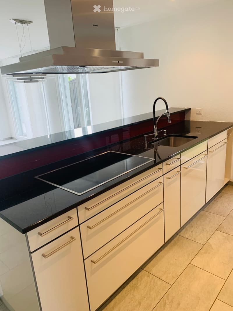 Modern kitchen with white cabinets, black countertops, a stainless steel range hood, and a built-in induction cooktop.