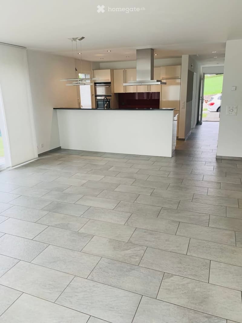 Open-plan kitchen and living area with modern cabinetry, stainless steel appliances, and a central island. The floor is covered with large, light grey tiles.