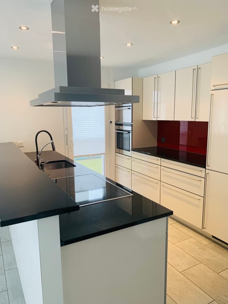 Modern kitchen with white cabinets, black countertops, stainless steel appliances, and a central island with a sink and stove.