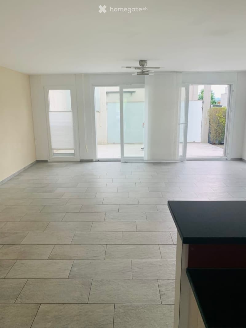 Empty room with tiled floor, large sliding glass doors leading to an outdoor area, and a ceiling fan.