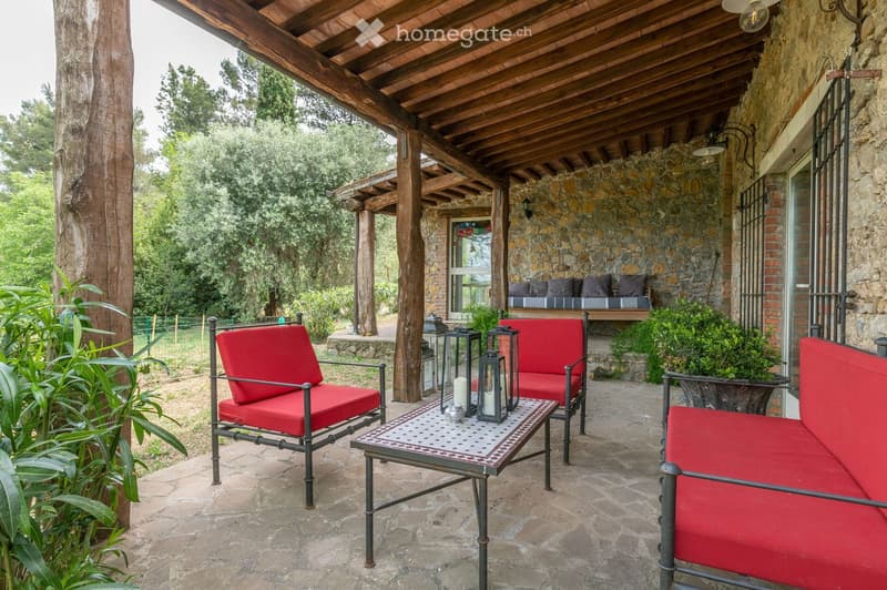 Outdoor patio with stone walls, wooden beams, red cushioned seating, lanterns, and a coffee table.