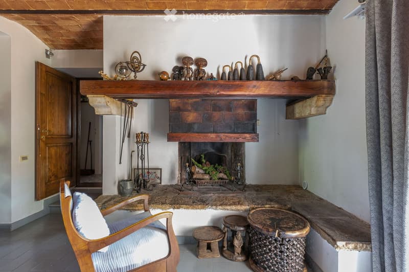 Living room with a stone fireplace, wooden mantel, decorative sculptures, a wooden chair, and small wooden stools.