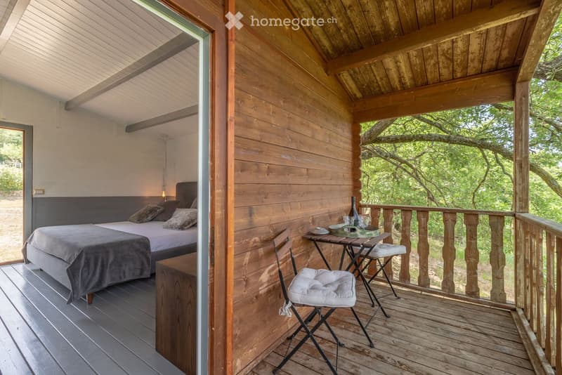 Wooden balcony with a small table, chair, and bottle, overlooking a lush green landscape.
