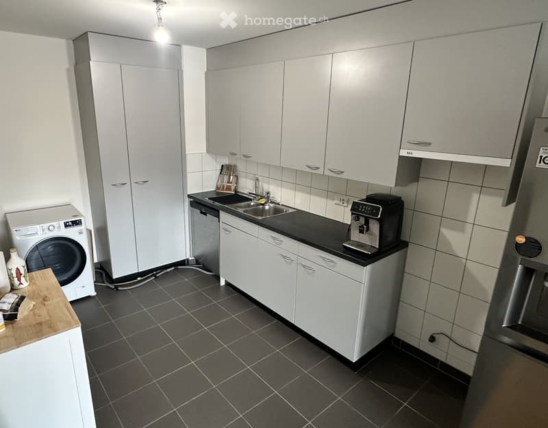 Modern kitchen with white cabinets, black countertops, stainless steel sink, dishwasher, coffee maker, and washing machine.