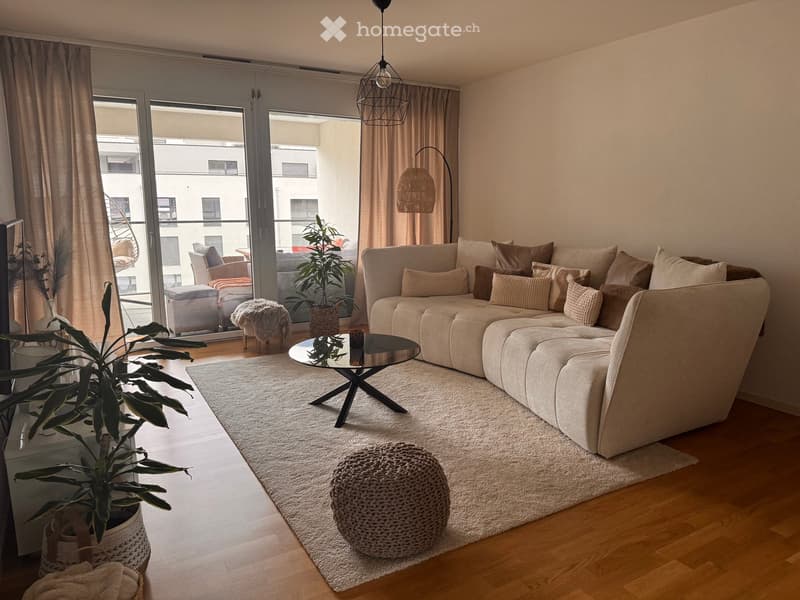 Modern living room with a large sectional sofa, coffee table, round stool, potted plants, and a view of a balcony area.
