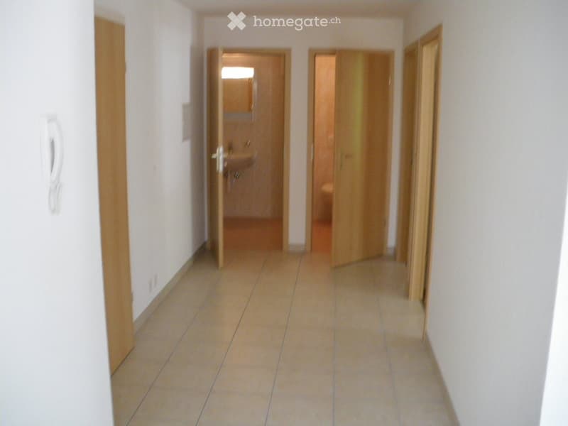 Empty hallway with tiled floor, white walls, and three open wooden doors leading to other rooms.