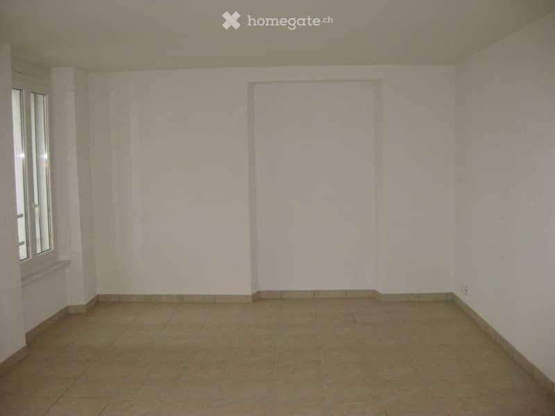 Empty room with tiled floor and white walls, featuring a window on the left side and a small shelf below it.