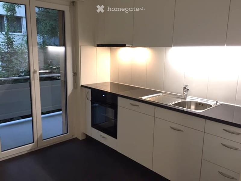 modern kitchen, white cabinets, granite countertops, integrated oven and dishwasher, stainless steel sink and faucet, sliding glass door to balcony
