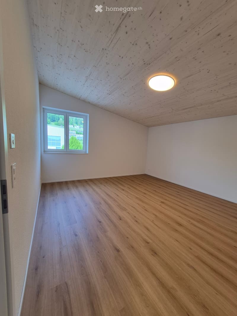 Empty room with wooden flooring, white walls, and a skylight window. The ceiling has exposed wooden beams and a recessed light fixture.