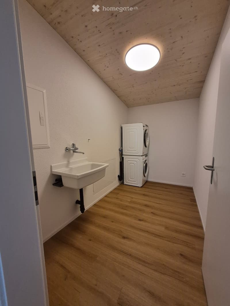 Small room with wooden flooring, white walls, a sink, and a stacked washing machine and dryer.