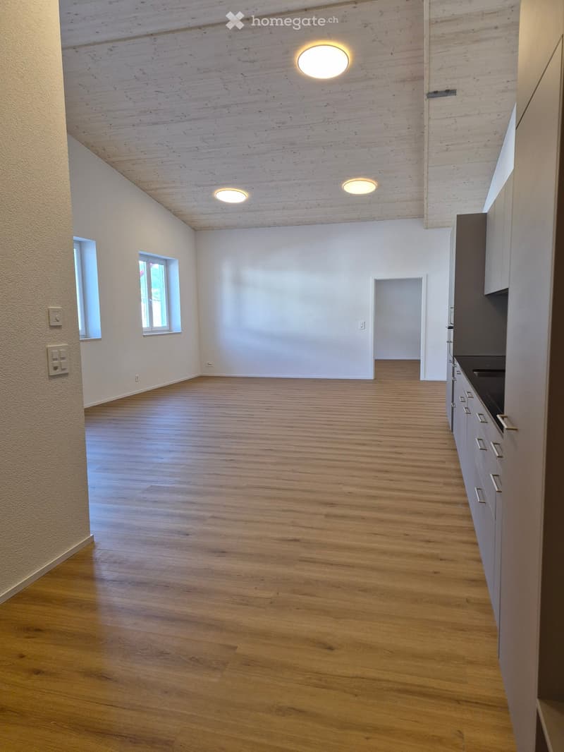 Empty room with wooden flooring, white walls, and recessed lighting. Features two small windows and a doorway leading to another space.