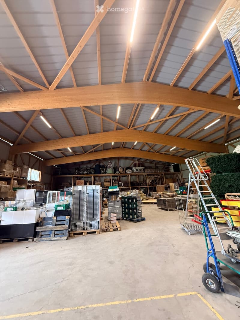 Large industrial-style warehouse with exposed wooden beams and metal shelving, filled with various stored items including appliances, boxes, and equipment.