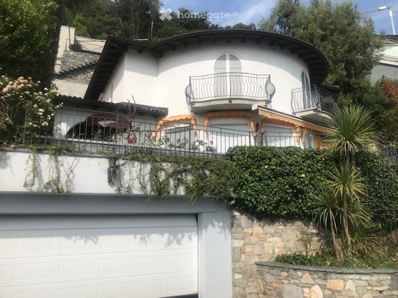 White painted house with black roof, garage on the ground floor, balcony on the second floor.