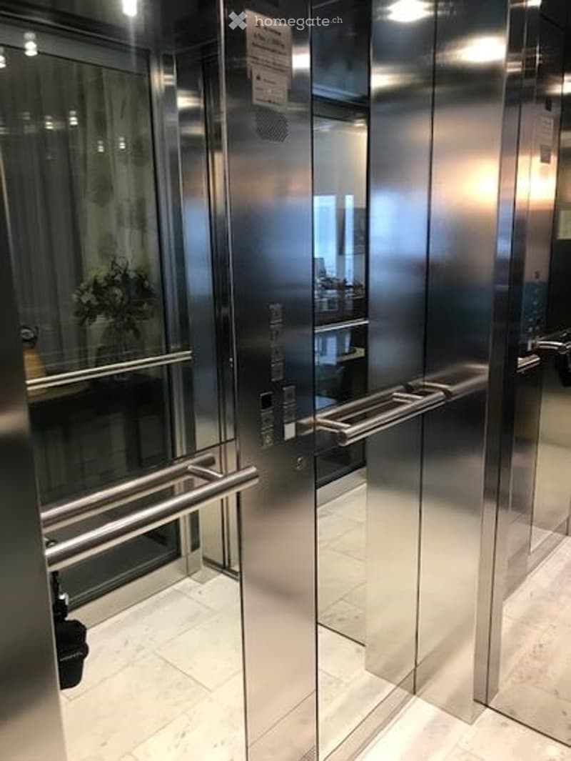Modern stainless steel elevator with glass walls, illuminated by ceiling lights, interior is clean and shiny