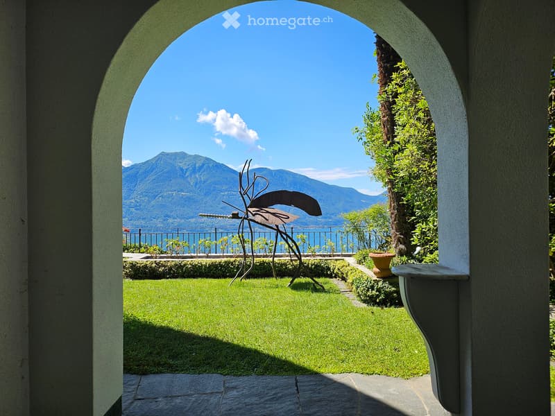 arch entrance, sculpture, grassy lawn, hedges, fenced view, mountains in the background