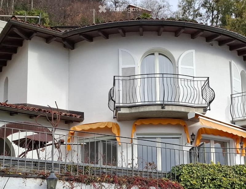 White exterior, brown tile roof, balcony with metal railing, large windows, awnings, white shutters