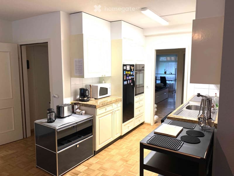 Modern kitchen with white cabinets, granite countertops, stainless steel appliances, and wooden flooring.