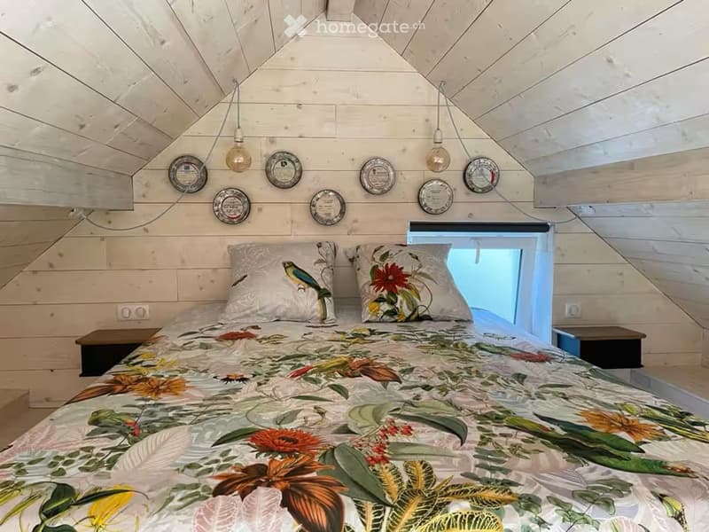 Cozy bedroom with wooden walls and slanted ceiling, featuring a large bed with floral bedding, two nightstands, and decorative plates on the wall.