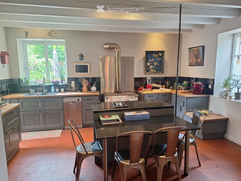 Modern kitchen with stainless steel appliances, wooden countertops, and a central island with a black countertop. The space includes a sink, stove, fridge, dishwasher, and various kitchen items on the counters.